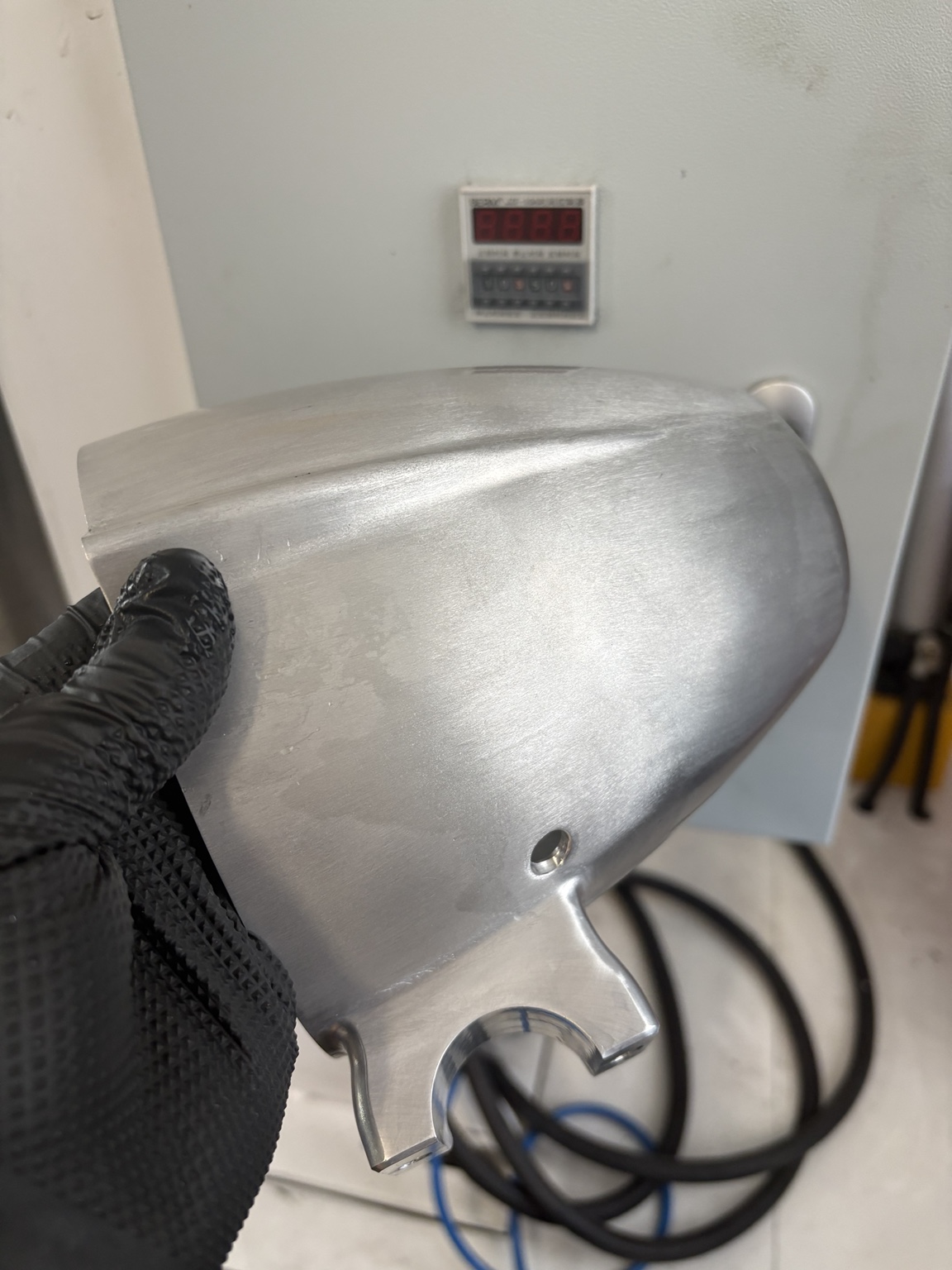Unfinished machined billet aluminum highway bar speaker housing held in a gloved hand, showing raw machining marks before finishing