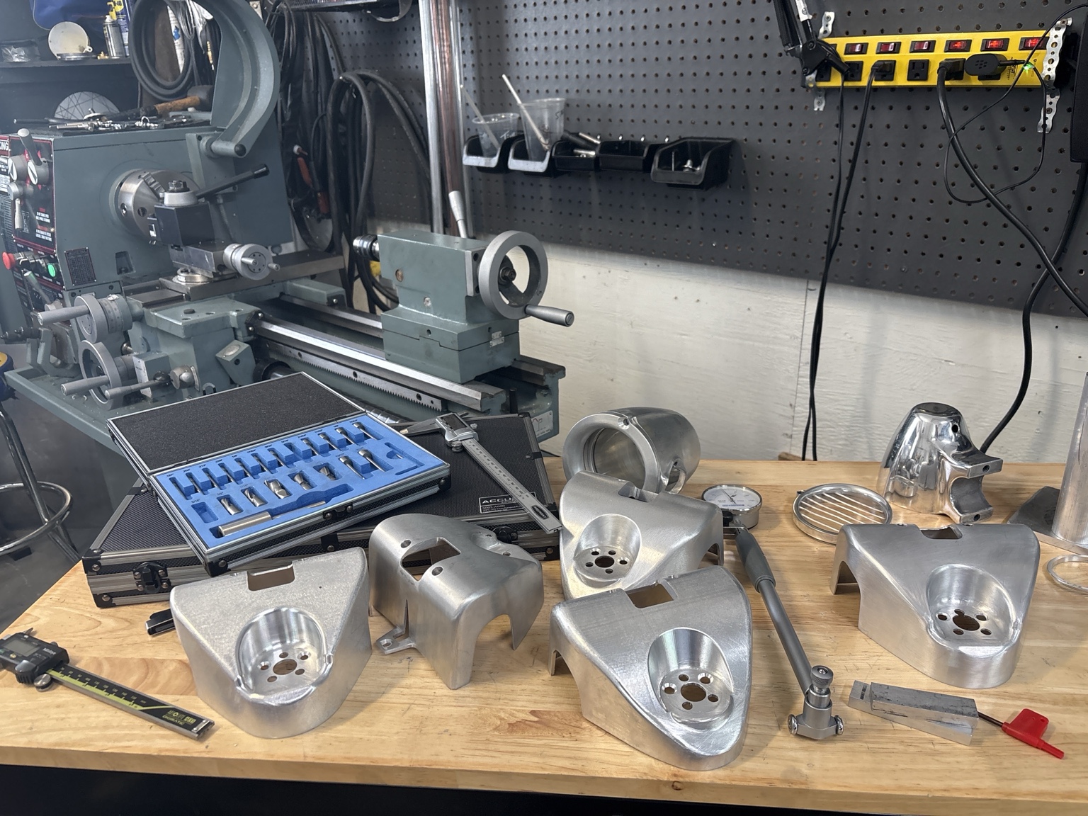 Workbench covered in machined billet stereo housings and speaker pods, with lathe tooling, dial indicators and calipers behind them