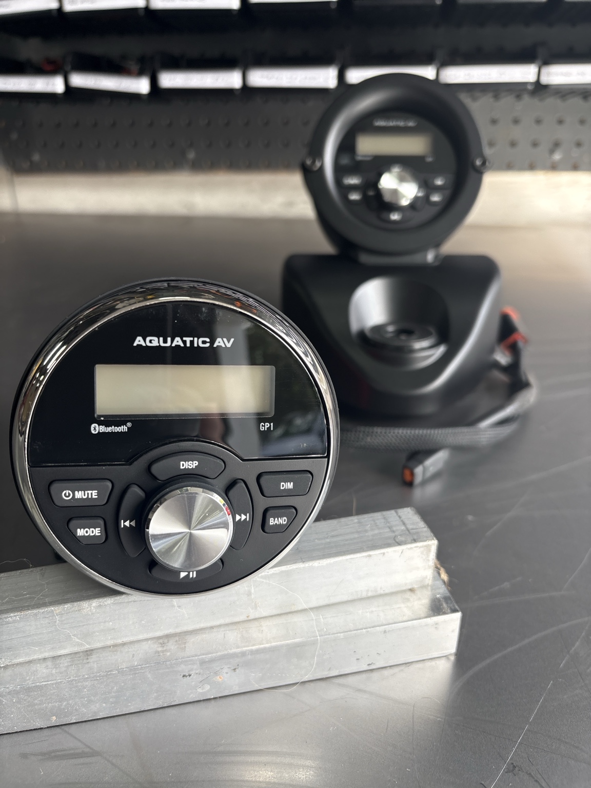 Aquatic AV GP1 head unit with its chrome bezel on the workbench beside a second GP1 installed in a black speaker pod housing