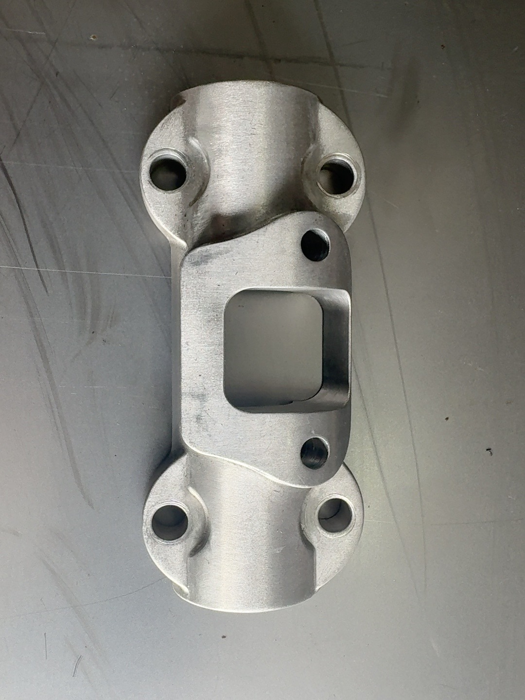 Raw machined Havoc Softail handlebar clamp with the parallel bolt pattern, lying on a scratched steel workbench