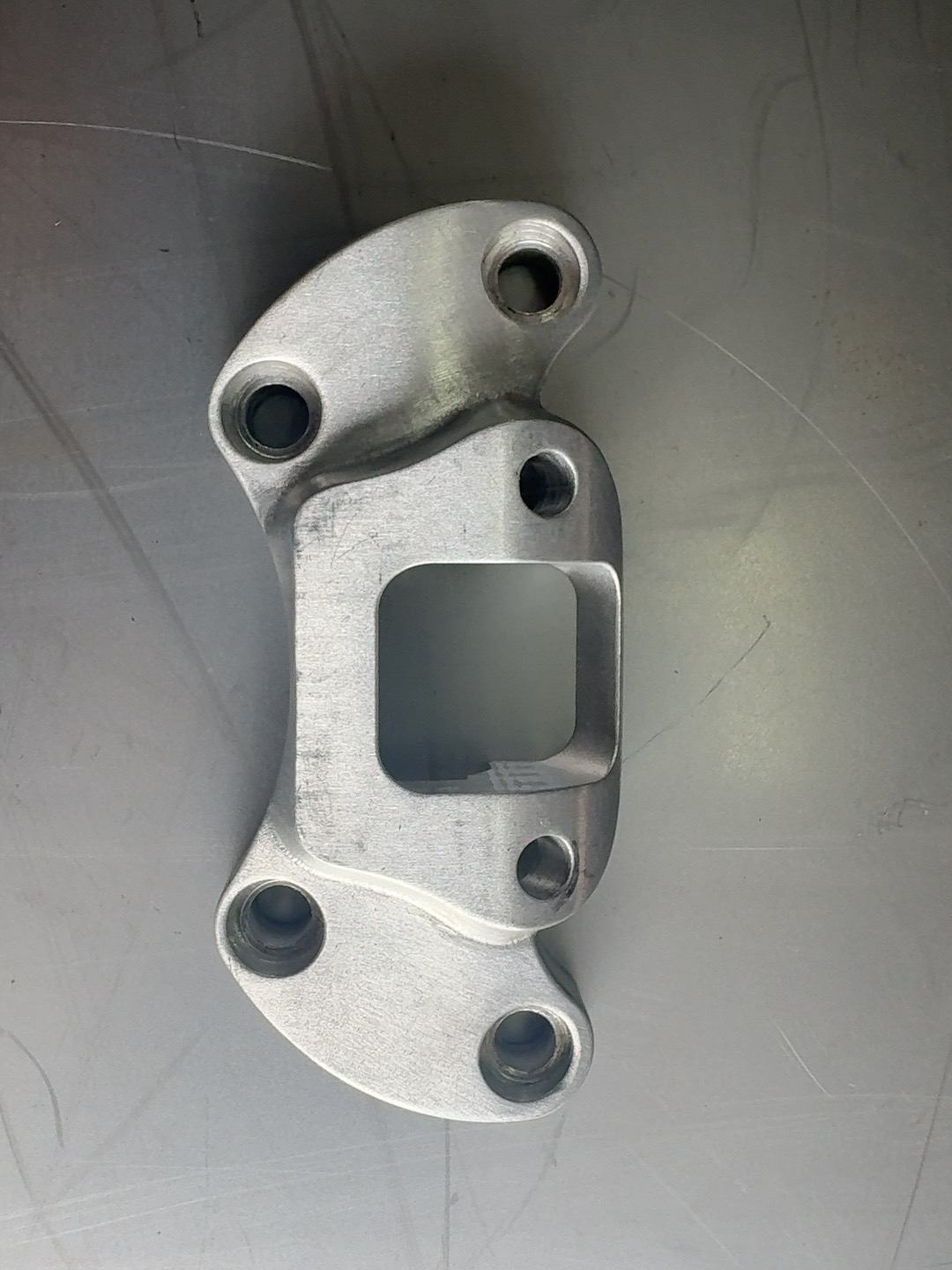 Raw machined Havoc Softail handlebar clamp with the offset bolt pattern, lying on a scratched steel workbench